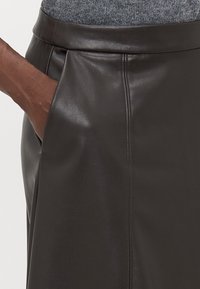 Gonna in pelle marrone scuro con un design sartoriale, texture liscia, tasca laterale e dettagli di cucitura discreti.