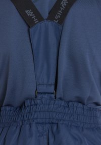 Gros plan sur un pantalon en tissu bleu avec une ceinture élastique et des bretelles noires attachées à l'avant.