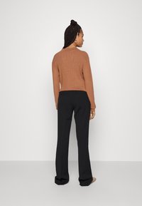 Hnědý svetr s ribbed vzorem a dlouhými rukávy, doplněný užšími černými kalhotami. Model je zobrazen zezadu na neutrálním pozadí.