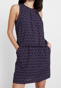 Ärmelloses navy blaues Kleid mit einem floralem Muster in Pink und Weiß. Verfügt über einen gefältelten Ausschnitt und Taschen im Rock. Weicher, leichter Stoff.