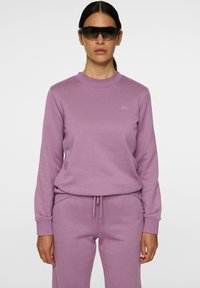 Felpa lilla con maniche lunghe e scollo rotondo, abbinata a pantaloni coordinati; presenta un logo discreto e una vita con coulisse.