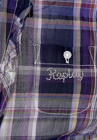 Kostkovaná košile v odstínech fialové, modré a zelené. Obsahuje přední kapsu s průhledným knoflíkem a detailem loga s rhinestones.