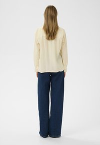 Lichtgele, langomarmige shirt met een geribbelde textuur en gebuttonde manchetten. Gepaard met losse, donkerblauwe spijkerbroek in een wijde pasvorm.