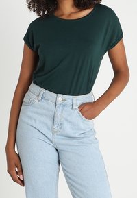 Mörkgrön kortärmad T-shirt kombinerad med ljusblå högmidjade jeans, med en åtsittande passform och mjukt tyg.