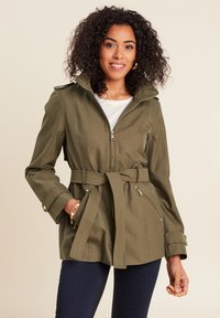 Olijfgroene jack met een ritssluiting aan de voorkant, capuchon en een ceintuur in de taille. Heeft zijzakken en ribbeldetails op de mouwen en de ceintuur.