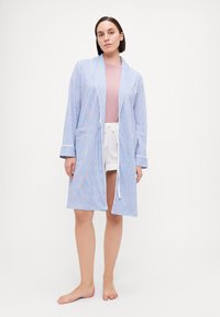 Blå och vit randig badrock med långa ärmar, breda slag och två framfickor; bärs över en rosa topp och vita shorts.