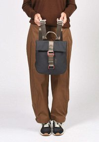 Mochila negra de tipo roll-top con correas ajustables grises, con hebilla en tono oro rosa. Tejido robusto con textura suave y detalle de logo.