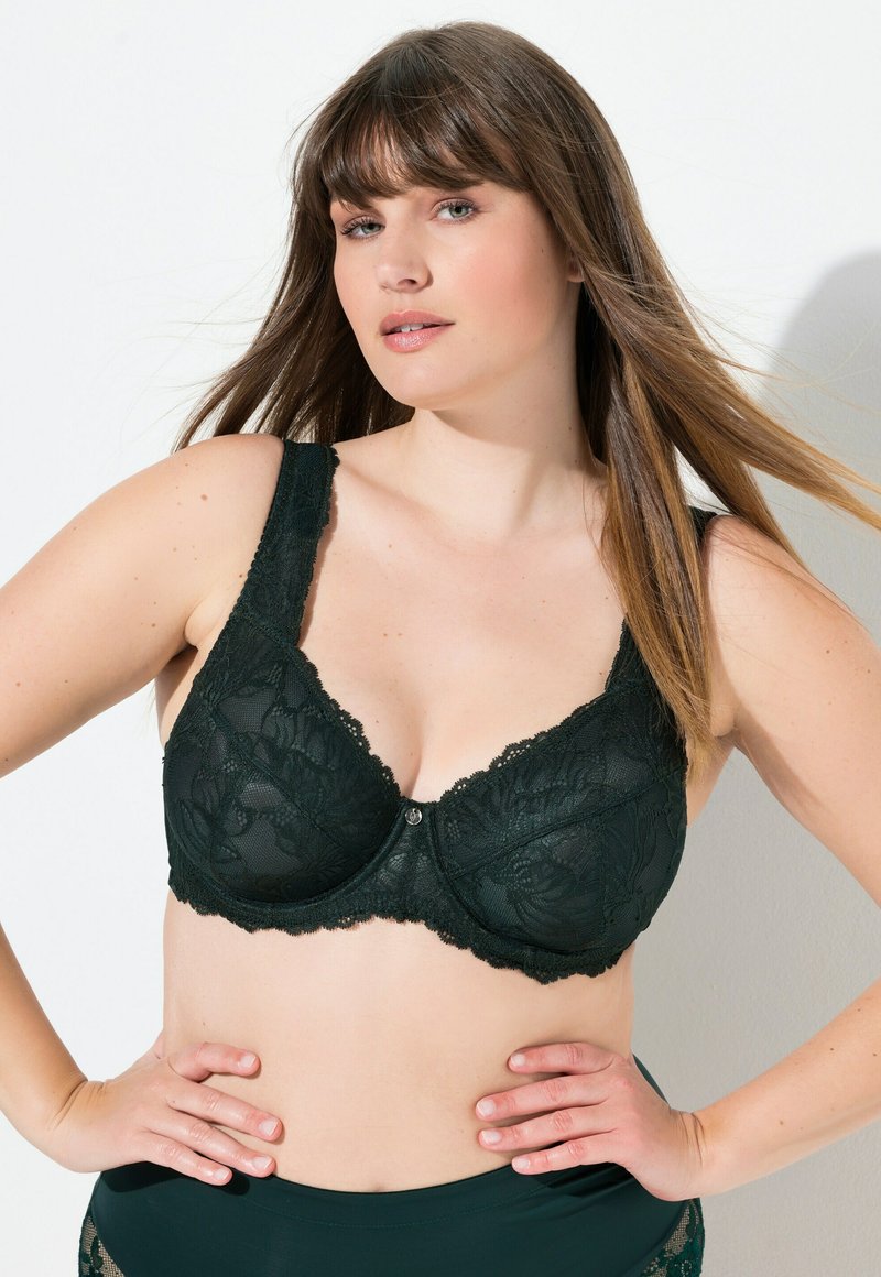 Tumman vihreä pitsirintaliivi, jossa on leveät pitsihihnat, kukkakuviot ja keskellä koristepainike. Pehmeä tekstiili ja tukeva johdinsulku.