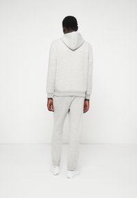 Pilka medvilninė džemperio striukė su reguliuojamu kapuci, raštuotais rankogaliais ir atitinkančiomis sportinėmis kelnėmis. Komplektas pasižymi minkšta tekstūra ir laisvu siluetu. Baltos sportbačiai.