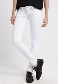 White skinny jeans made of stretch fabric with five-pocket design, belt loops, and subtle stitching details, paired with black shoes.