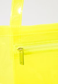 Transparent gul farge tote veske med glidelåslomme, gullfarge detaljer og teksturert overflate. Lys og lett design.