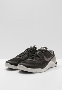 Mustat urheilukengät, jotka on valmistettu verkosta ja synteettisistä materiaaleista, harmailla yksityiskohdilla ja tekstuurilla varustetulla pohjalla. Nauhat ovat mustia, joissa on heijastavia elementtejä.