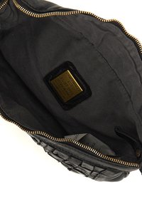 Interno di una borsa in pelle nera con un motivo testurizzato, zip dorata e etichetta del marchio. Rivestita con tessuto nero, caratterizzata da una finitura liscia.