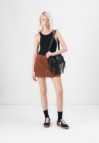 Black sleeveless top, brown corduroy mini skirt, black crossbody bag with fringe detailing, and black sneakers with cream accents.