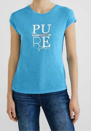 Osoba nosząca niebieski t-shirt z krótkim rękawem z białym napisem "PURE soul" i podwiniętymi mankietami, w połączeniu z ciemnoniebieskimi jeansami na jednolitym jasnym tle.