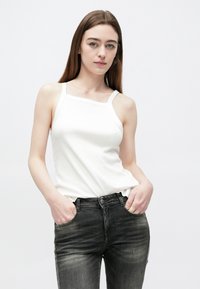 Biele priliehavé tielko s tenkými ramienkami a textúrovaným povrchom, skombinované s tmavosivými džínsami s miernym vyblednutím a bočnými vreckami.