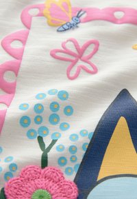 Színes anyag, amely fehér alapon rózsaszín, kék és zöld virágmintákat, texturált elemeket és egy pillangó mintát tartalmaz.