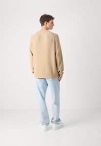 Beige ribbed knit sweater with a relaxed fit, featuring a crew neckline and drop shoulder seams, paired with light blue straight-leg jeans.