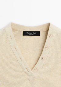 Maglione in maglia a coste beige con scollatura a V, caratterizzato da quattro bottoni su un lato e un'etichetta con la scritta "Massimo Dutti, Made in China."