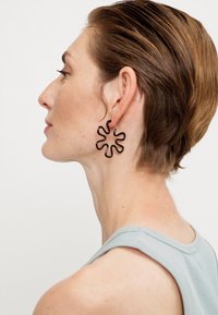 Schwarze, wellenförmige Ohrringe aus leichtem Material mit einem strukturierten Design, das abstrakten Blütenblättern ähnelt.