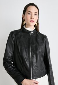 Svart läderjacka med en kortad design, hög krage och dragkedja fram. Har sömnadsdetaljer och en jämn textur.