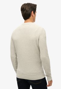 Licht beige gebreide trui met een gestructureerd patroon, ronde halslijn en ribgebreide manchetten en zoom, gedragen met donkerblauwe jeans.