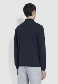 Námořnické modré polo tričko s dlouhým rukávem z bavlněné směsi, s klasickým límečkem a zadním sárem, v kombinaci s světle šedými tepláky.