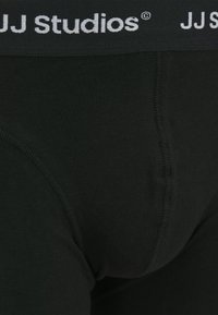 Schwarze Baumwollslips mit einem breiten grauen elastischen Bund, der das Logo "JJ Studios" trägt. Glatte Textur und verstärkte Nähte.
