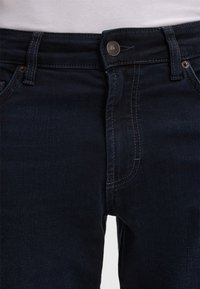 Jeans in denim blu scuro con un design aderente, cuciture visibili e una chiusura con bottone metallico in vita.