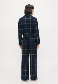 Merihenkinen ruudullinen yöpuku, jossa on pitkät hihat, joustava vyötärö ja leveät housut. Sisältää vihreän ja vaaleansinisen ruutukuvion. Pehmeä kangas.