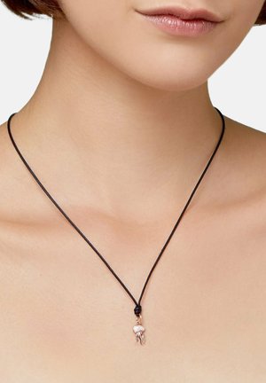 Close-up of a person wearing a black cord necklace with a small jellyfish-shaped pendant resting at the base of the neck.