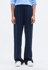 Φαρδιά παντελόνια σε ναυτικό μπλε από μαλακό ύφασμα, με πιέτες, ελαστική μέση και συνδυασμένα με λευκά αθλητικά παπούτσια.
