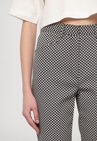 Pantalon navy à motif, présentant de petites fleurs beiges, coupe slim, en tissu texturé avec des poches latérales, associé à un top blanc cropped.