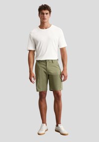 Weißes Kurzarm-T-Shirt, kombiniert mit olivgrünen Cargo-Shorts mit Seitentaschen, getragen mit weißen Sneakers und einer Gummisohle.
