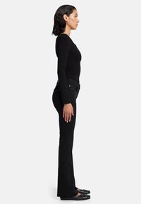 Zwarte langmouwtop gecombineerd met zwarte flared jeans en platte zwarte schoenen. De stof lijkt glad, met een getailleerd silhouet.