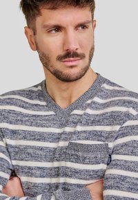 Jersey de pico con franjas horizontales en azul marino y blanco, tejido de punto texturizado y un bolsillo en el pecho con una etiqueta azul.