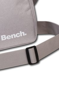 Graue Canvas-Schultertasche mit strukturierter Oberfläche, verstellbarem Träger und einem weißen "Bench."-Logo auf der Vorderseite. Hat ein schlankes, rechteckiges Design.