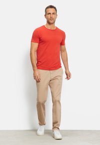 Rotes T-Shirt mit kurzen Ärmeln und rundem Halsausschnitt, kombiniert mit beigen Hosen und weißen Sneakers, die ein lässiges Outfit ergeben.