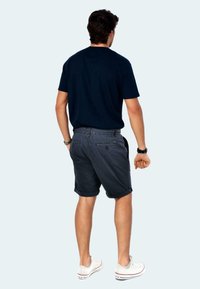 Dunkelblaue T-Shirt mit kurzen Ärmeln, kombiniert mit dunkelgrauen Shorts. Das Model trägt weiße Sneaker und steht in einer neutralen Haltung.