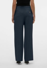 Wijde broek in donkerblauwe stof, met een soepele textuur, twee achterzakken en een knoopdetail bij de tailleband.