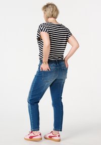 Jeans en denim bleu avec une coupe fuselée, dotés d'une taille élastique, de deux poches arrière et d'une chemise rayée décontractée. Des baskets roses complètent le look.