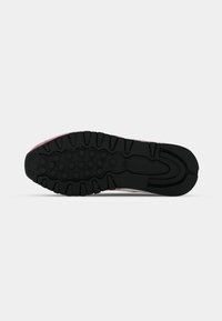Sola de borracha preta com textura e adesão, apresentando detalhes em rosa e a marca Reebok. Forma ligeiramente curvada, projetada para conforto e tração.