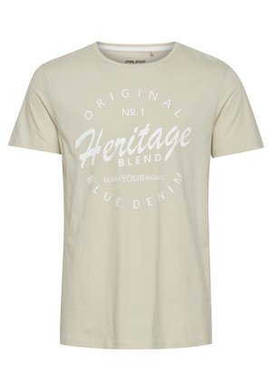 Beige bomull t-skjorte med rund hals. Har en stor hvit grafisk trykk med teksten "Heritage Blend" og tilleggs tekst, kortermet.