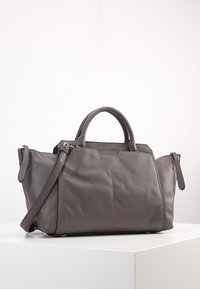 Mörkgrå läderhandväska med två handtag, avtagbar axelrem och zippered sidofack på vit plattform.