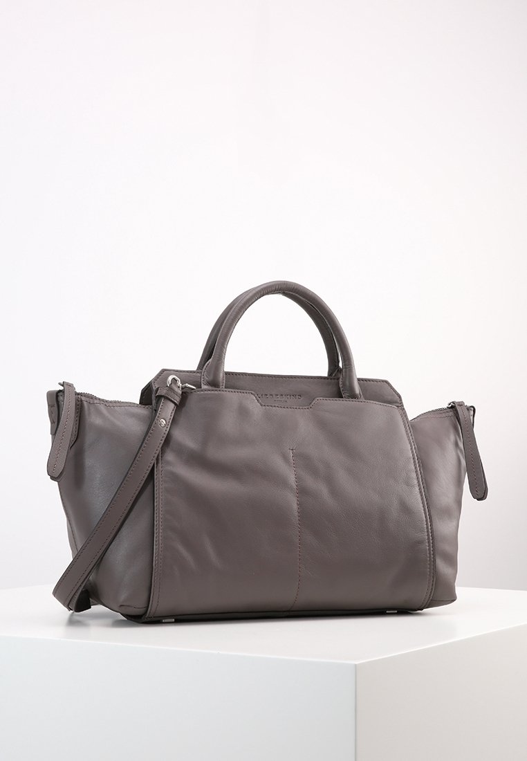 Mörkgrå läderhandväska med två handtag, avtagbar axelrem och zippered sidofack på vit plattform.