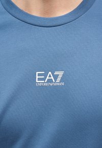 Blauw shirt met ronde hals en wit EA7 Emporio Armani-logo vlak in het midden van de borst.