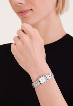 Zilveren polshorloge met een vierkante wijzerplaat, metalen schakelarmband en een minimalistisch ontwerp. Het horloge heeft een witte wijzerplaat en eenvoudige uurmarkeringen.