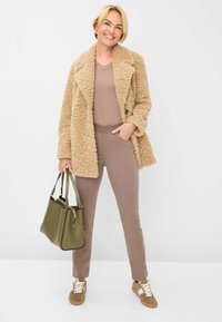 Beige faux fur frakke, brun tætsiddende top, brune bukser, olivengrøn håndtaske og brune sneakers med hvide snørebånd, stylet til et afslappet look.