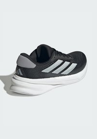 Baskets de sport noires avec une tige en mesh texturé, accents gris, trois rayures blanches sur le côté et une semelle rembourrée blanche.