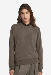 Brunstickad tröja med rund halsringning och ribbade ärmslut, kombinerad med en svart skjorta med krage. Mjuk textur, avslappnad passform och enhetlig färg.